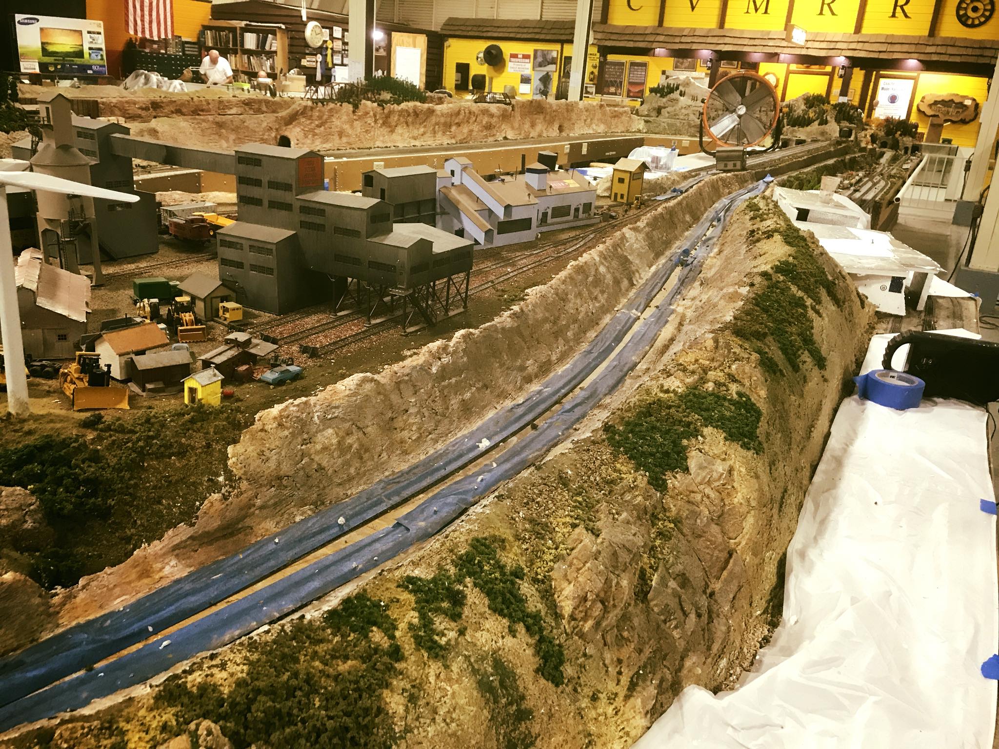 Detailed model train landscape featuring industrial buildings, a railway track, and a winding road, showcasing craftsmanship in miniature scene design.