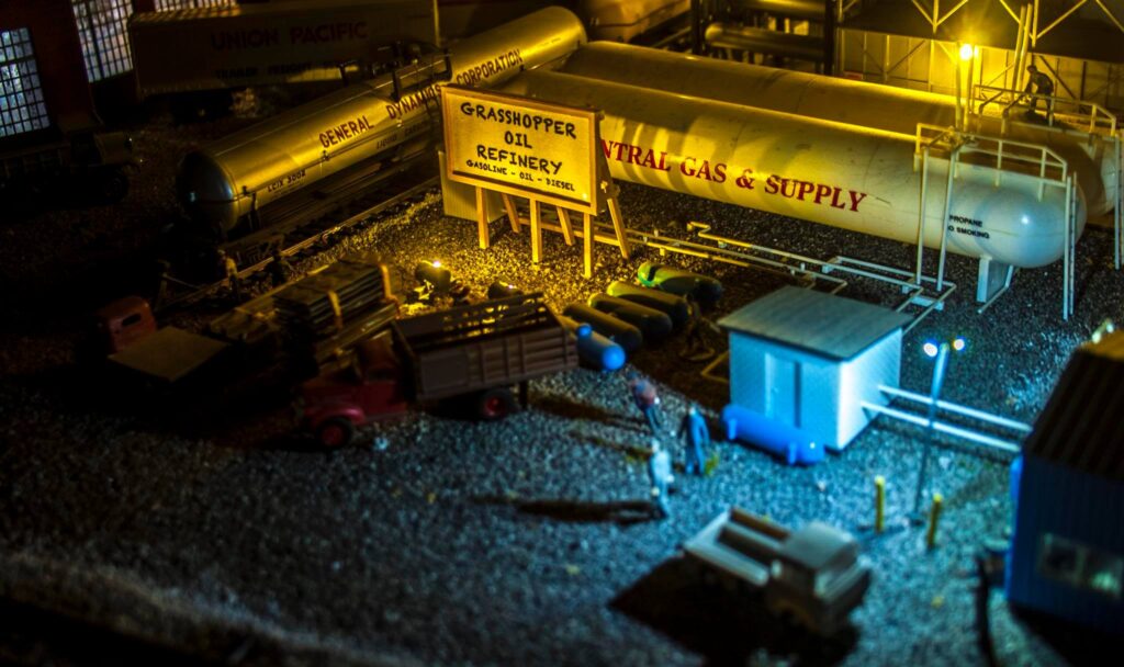 Miniature Grasshopper Oil Refinery scene featuring large storage tanks, trucks, and figures, illustrating a model industrial setting.