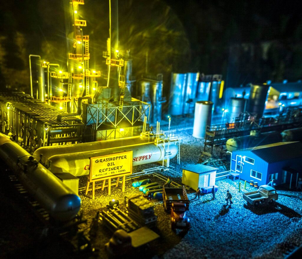 Detailed miniature model of the Grasshopper Oil Refinery, featuring tanks, pipes, and tiny figures, illustrating industrial activity and design.