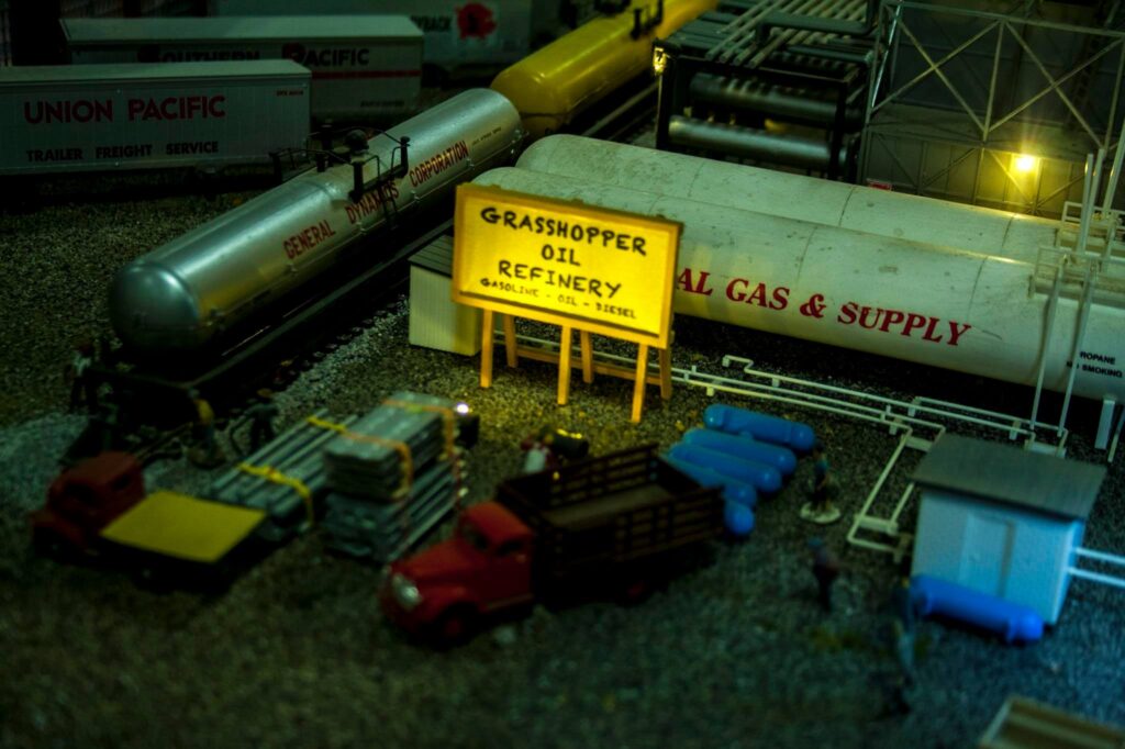 Grasshopper Oil Refinery model showcasing tanks, trucks, and a sign indicating fuels available. Highlights oil industry representation in miniature.
