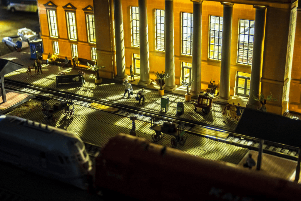 Model train station scene with illuminated building, figures waiting, and train tracks in use. Highlights the intricate details of railway culture.
